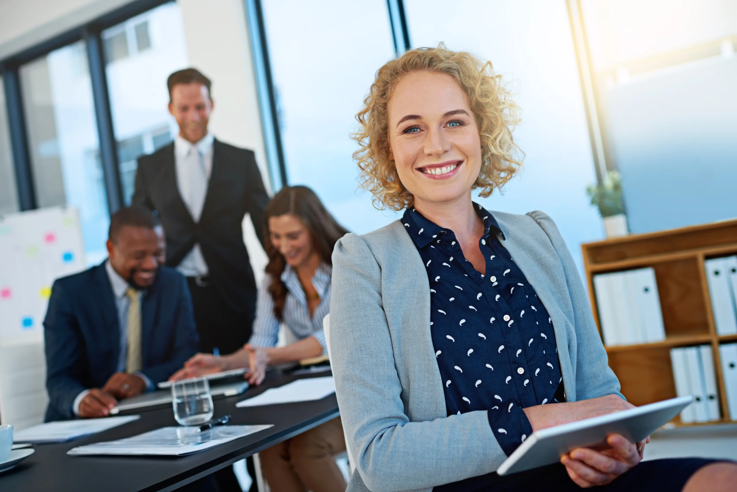 female HR Manager with blonde curly hair holding paperwork in an office setting